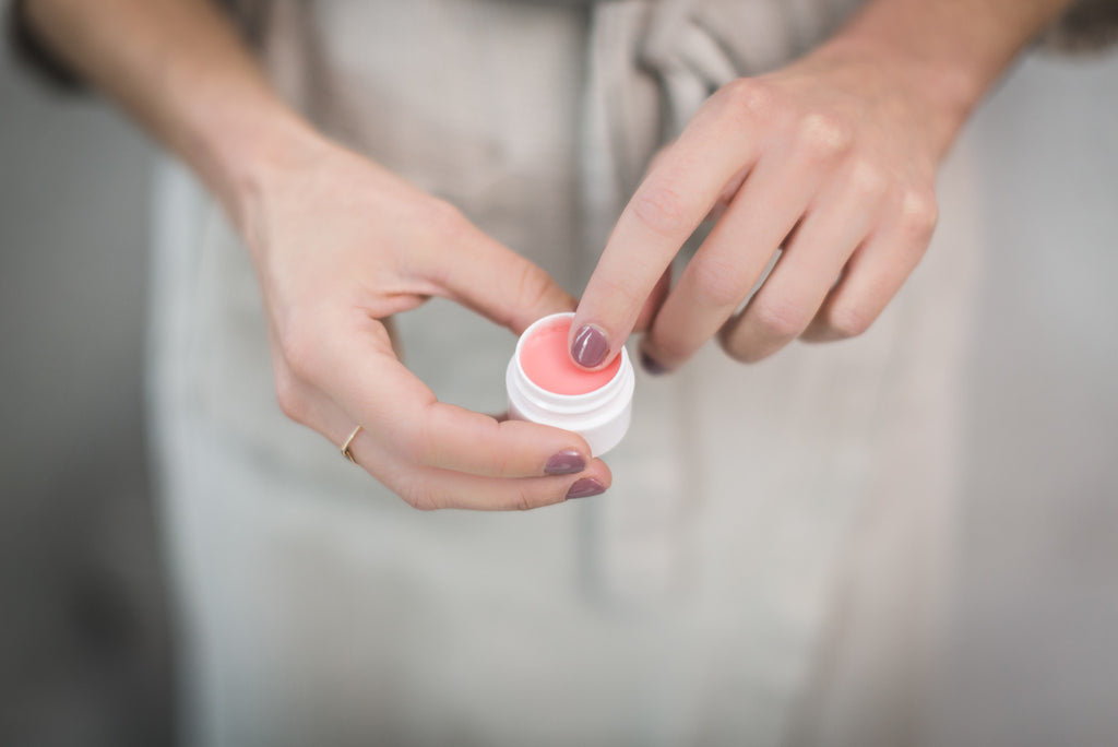 Hands holding jar of pink lip balm