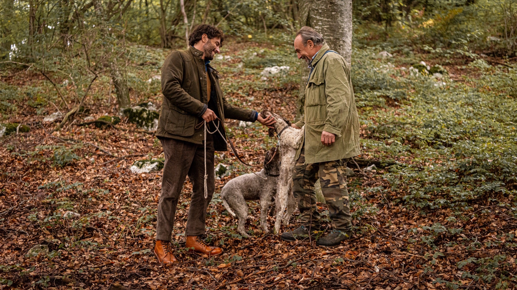 Two men walking their dog in the woods while wearing shoes by Velasca. 