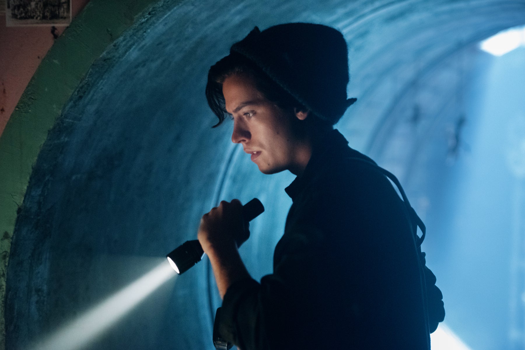 Jughead Jones investigates a dark tunnel holding a flashlight.