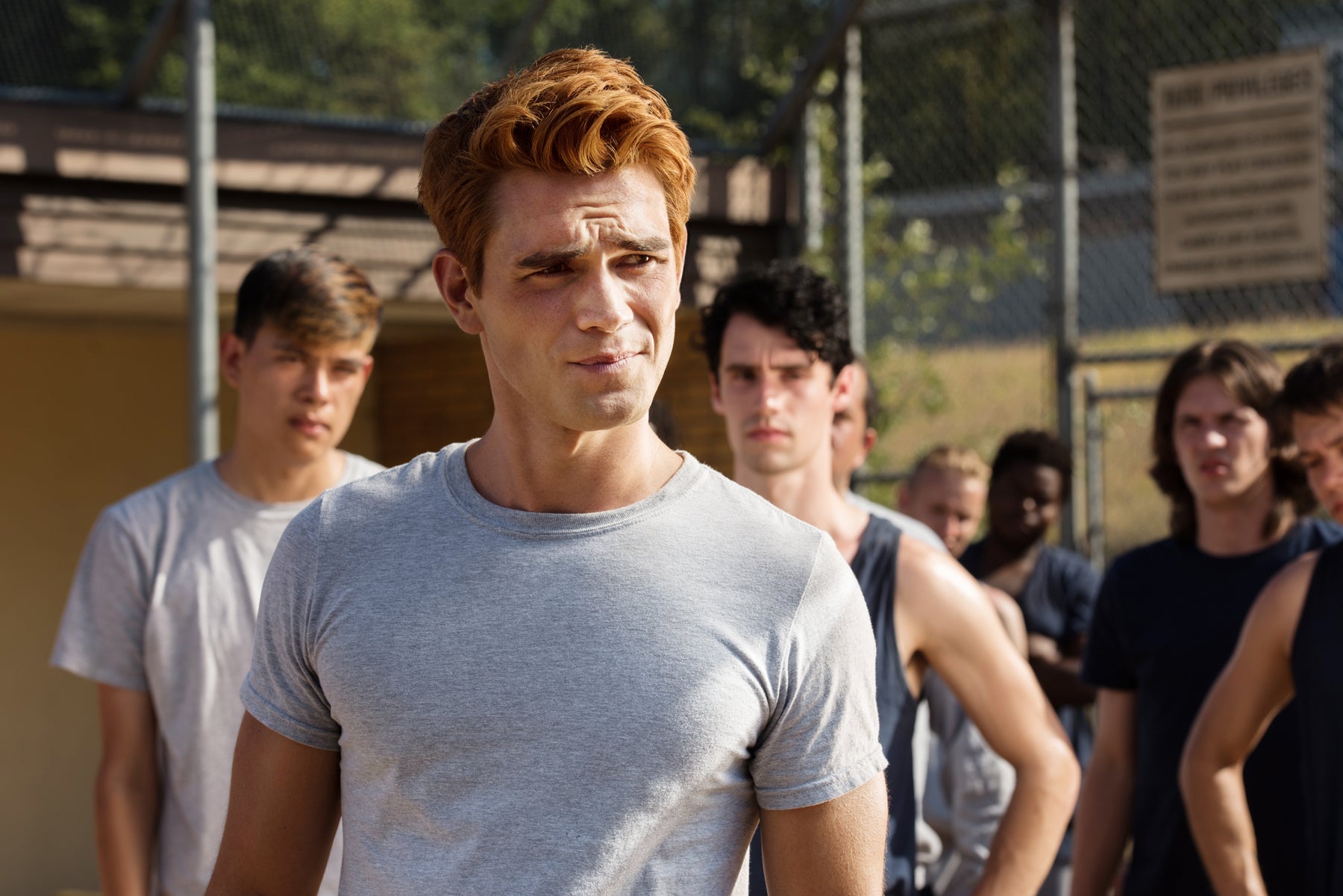 Archie Andrews looks off camera while fellow inmates stand behind him.
