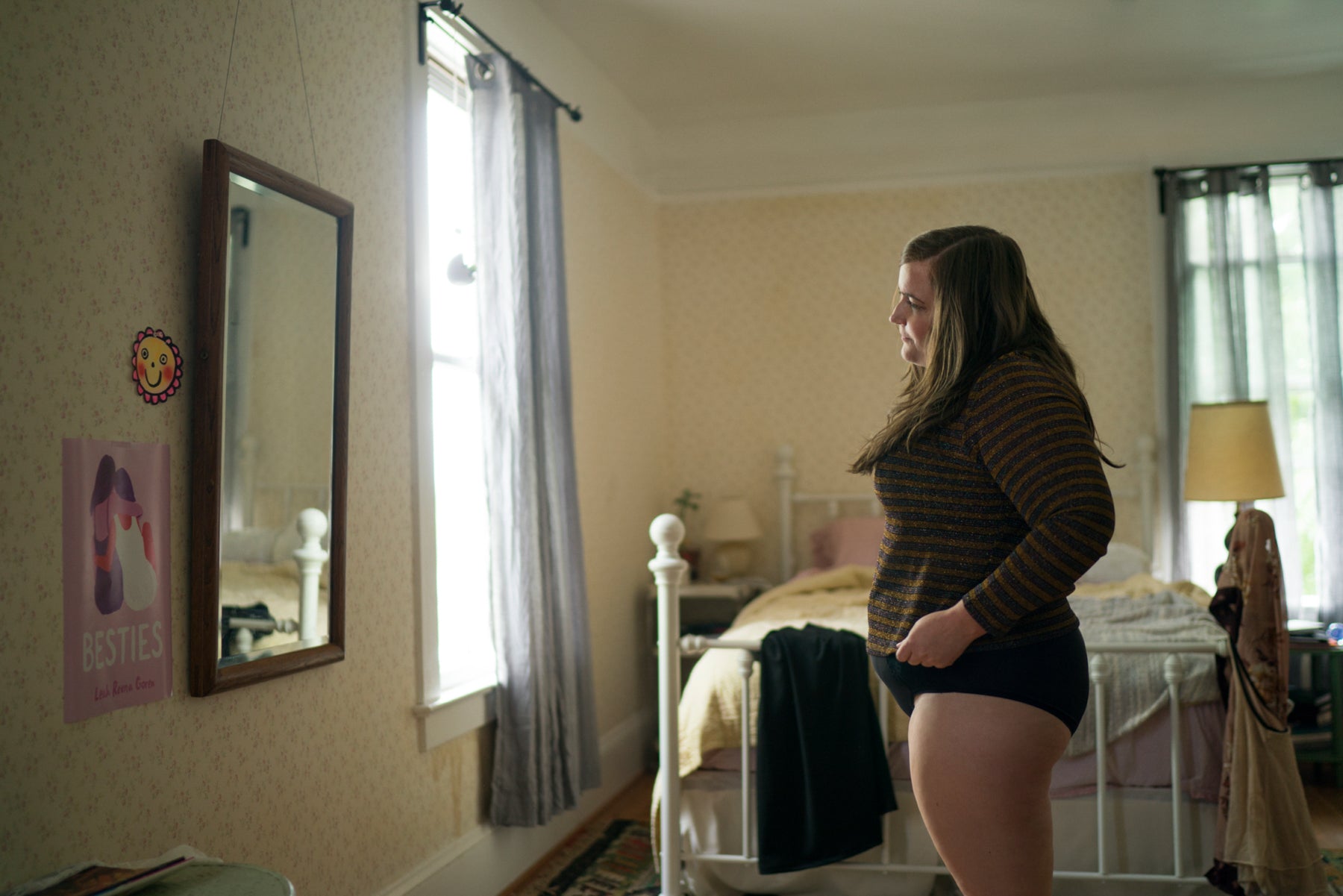 Annie (Aidy Bryant) looks at herself in the mirror. She looks quizzical and unhappy.  