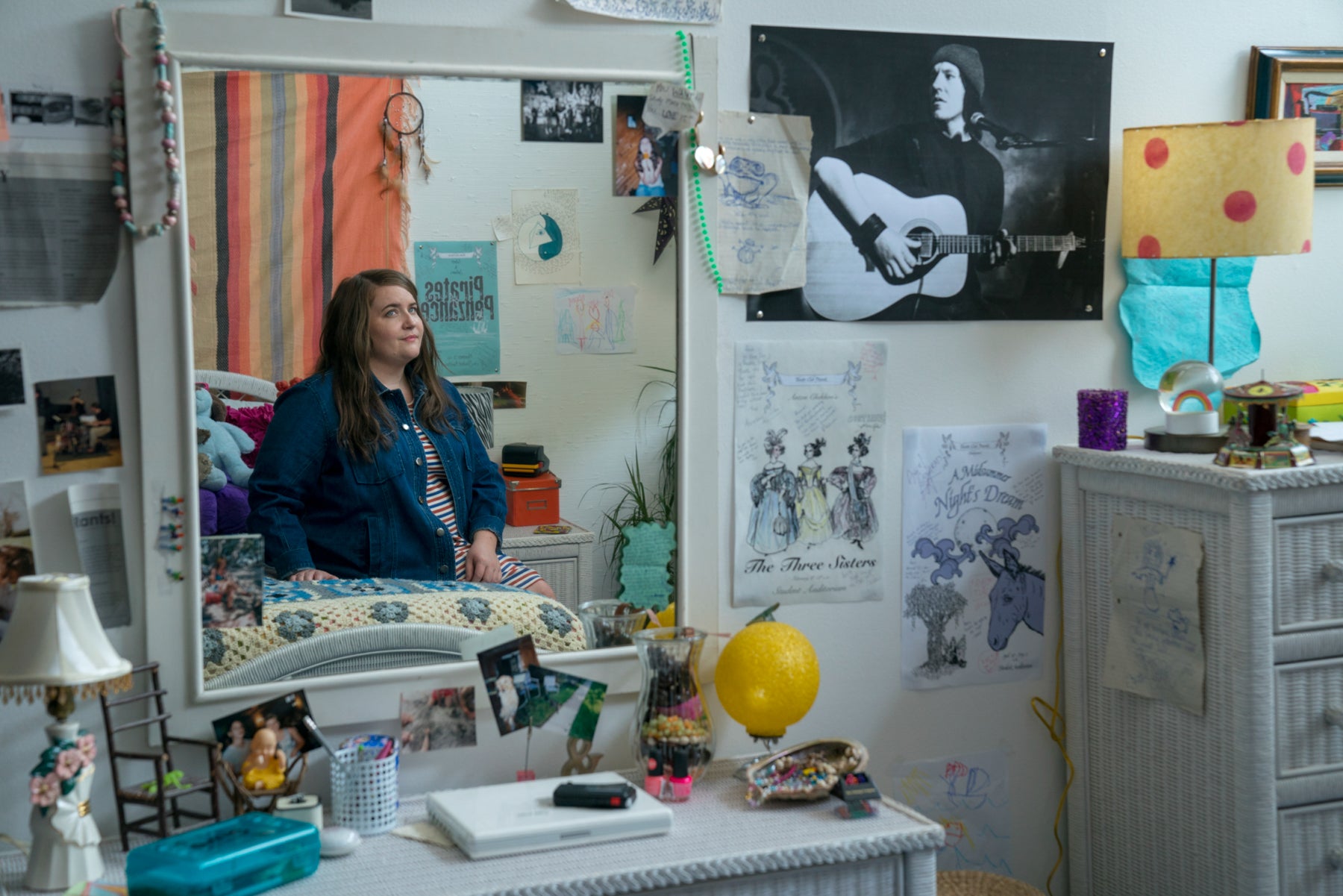 Annie sits on her bed in her childhood bedroom and is reflected in a mirror. 