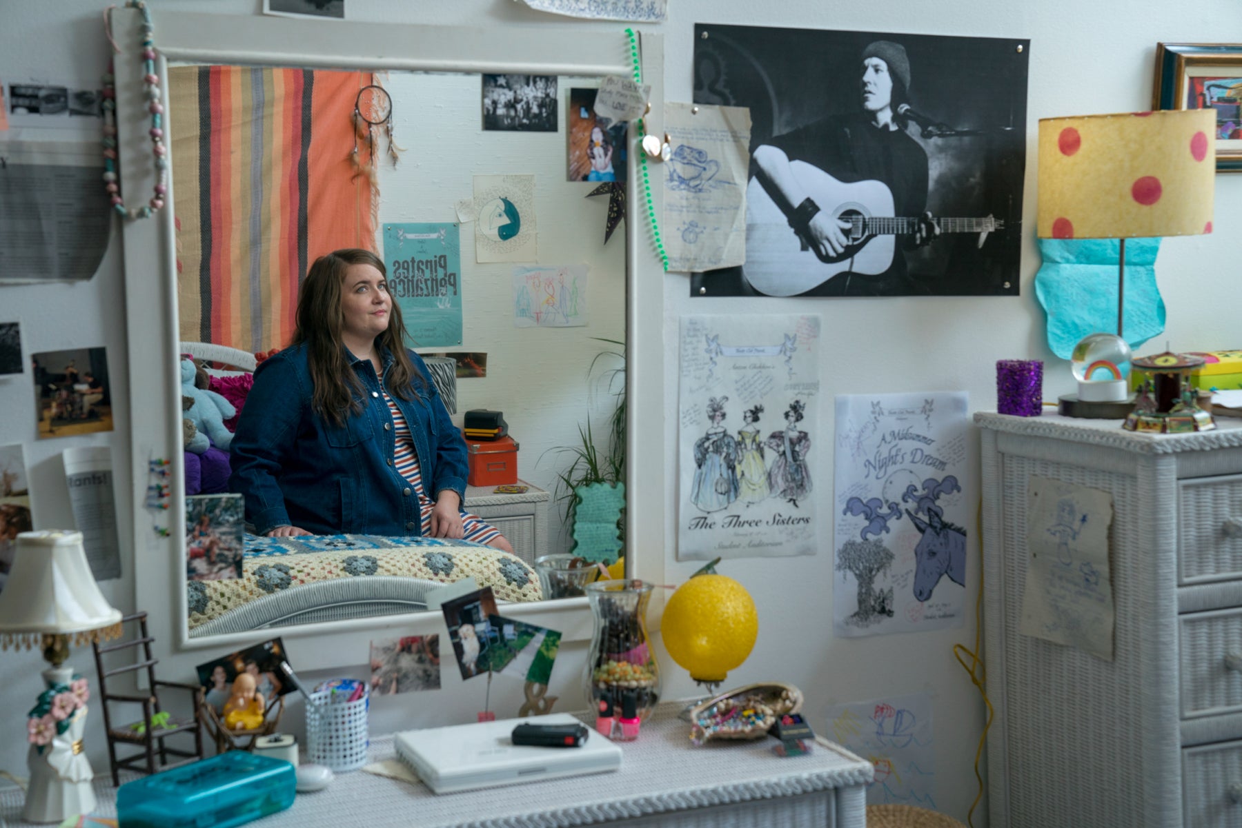 Annie sits on her bed in her childhood bedroom and is reflected in a mirror.