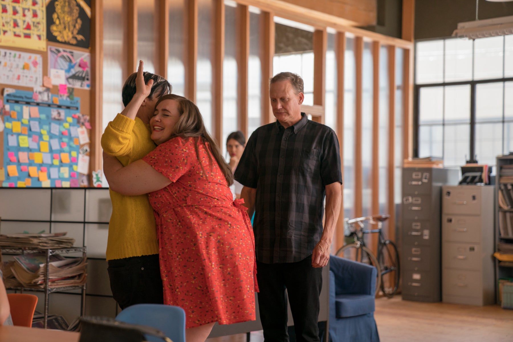 Annie hugs her boss in a scene from Shrill, but he doesn’t seem to want the hug and is standing stiffly with his arms raised. 