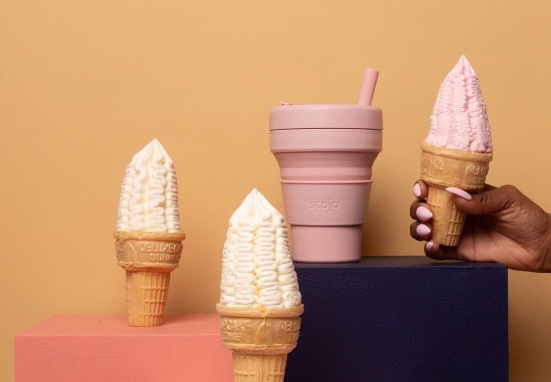 A Stojo cup is staged with a hand holding ice cream and other freestanding ice cream cones