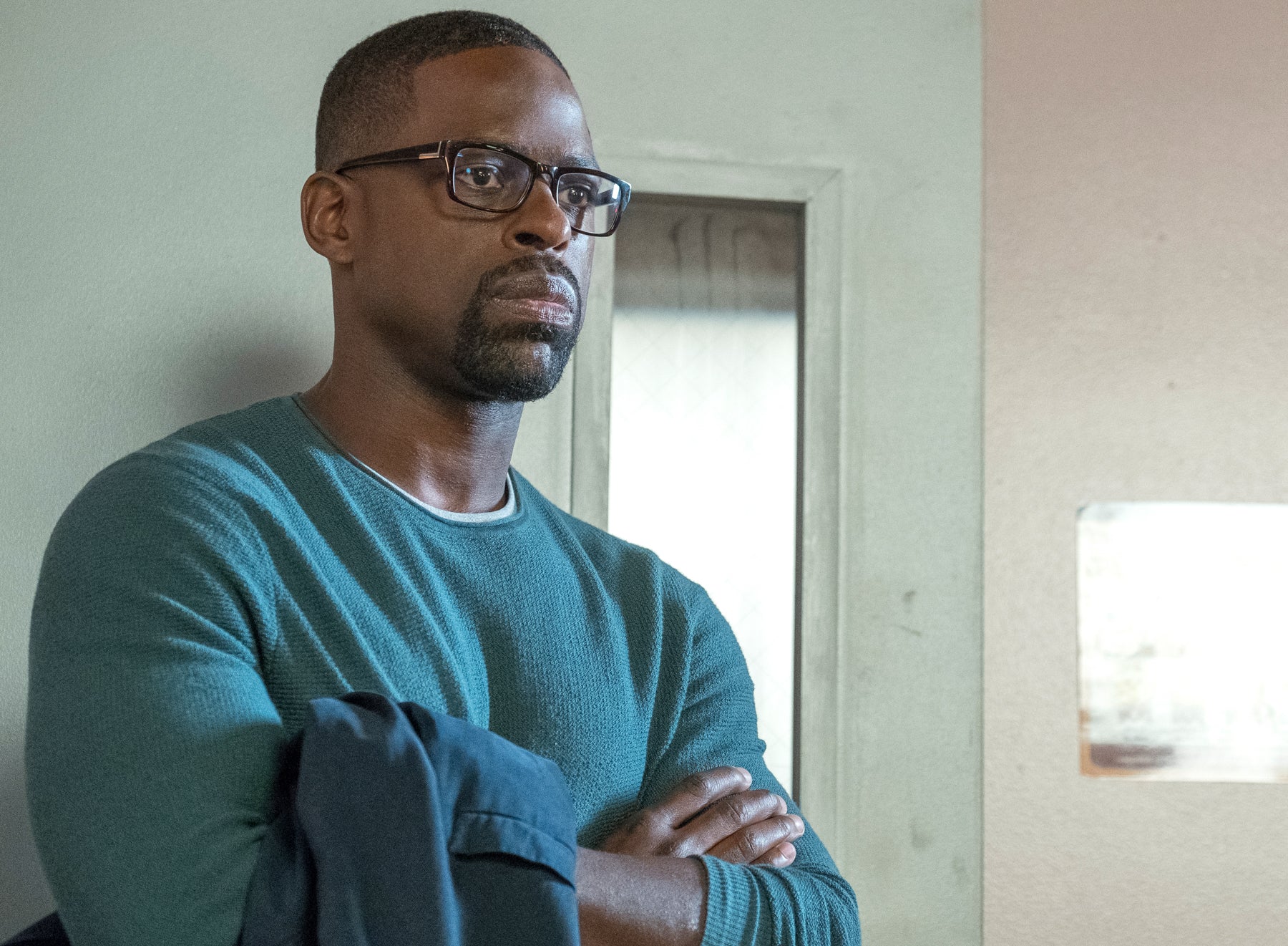 Randall Pearson (Sterling K. Brown) stands leaning against a mint door, looking off camera with a serious expression in an episode of This Is Us.