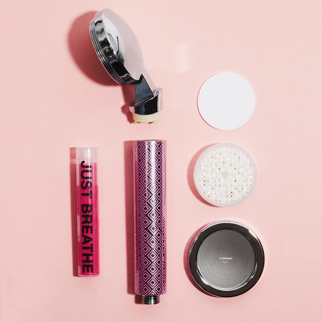 The components of a Vitaclean shower head in a flat lay on a pink surface