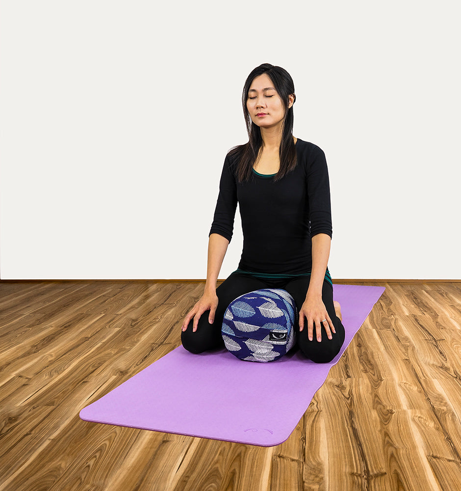 In Sukhasana, settle the sit bones toward the front edge of the bolster.