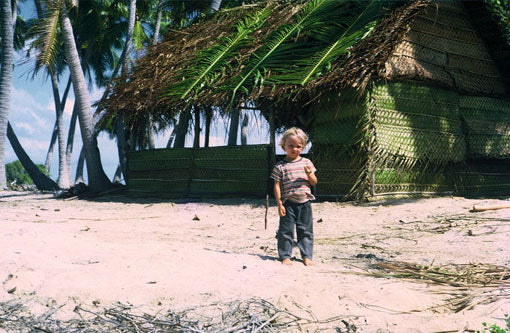 2 year old Josh Humbert on Ahe standing in front of a traditional Tahitian house. You can tell the house is newly built because the palm fronds used in the construction are still green.