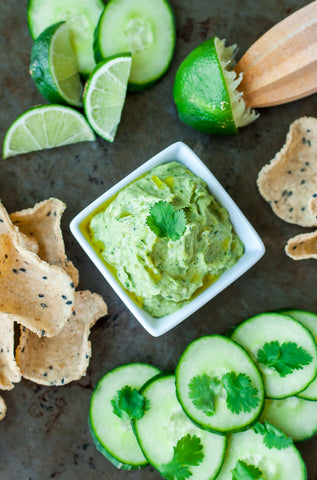 white bean dip with avocado and cilantro in a white bowl surrounded by limes