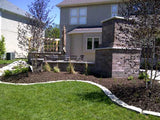 A serpentine rock border separates grass from a bed newly planted with shrubs and ground cover.