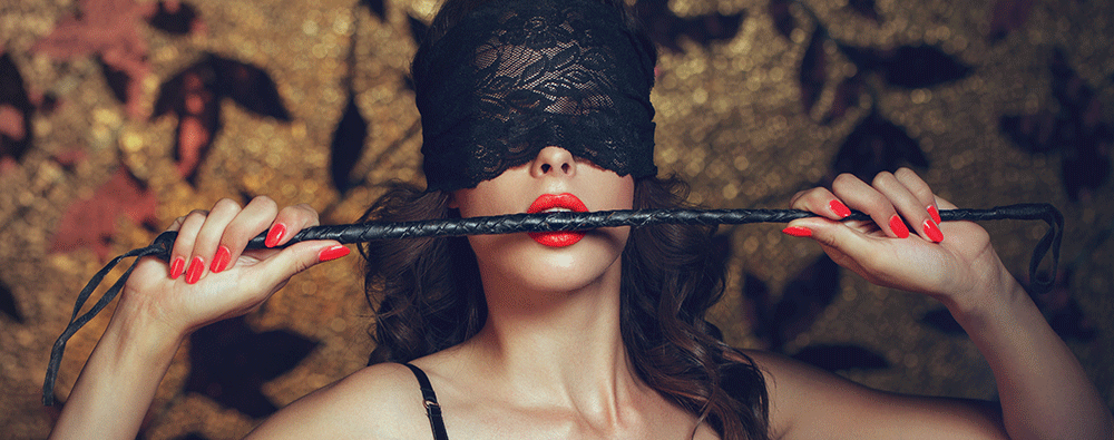 a woman wearing a black lace blindfold biting a whip