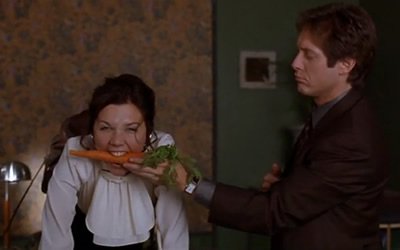 Image of man holding carrot and woman biting down on it