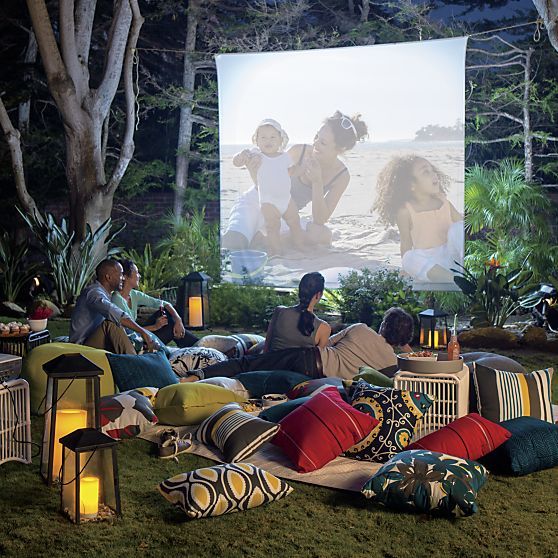 people sat on grass with cushions and image projected onto white sheet in trees
