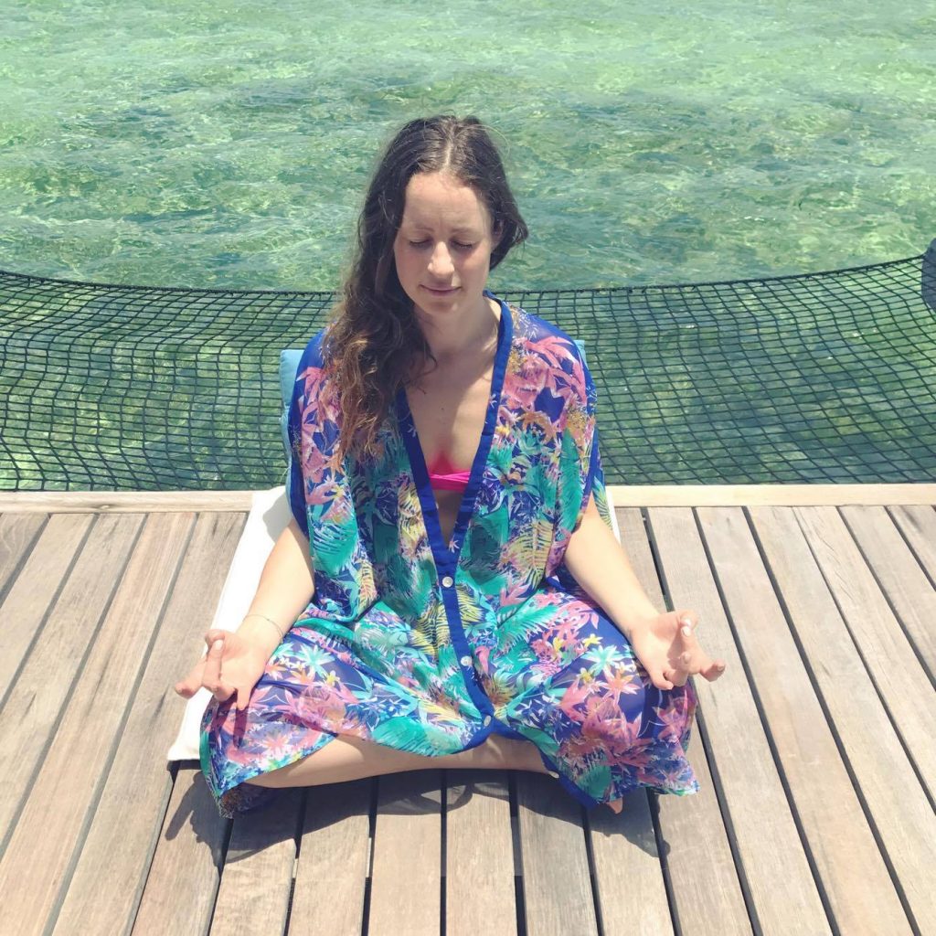 Jody Shield meditating on a wooden balcony above the sea