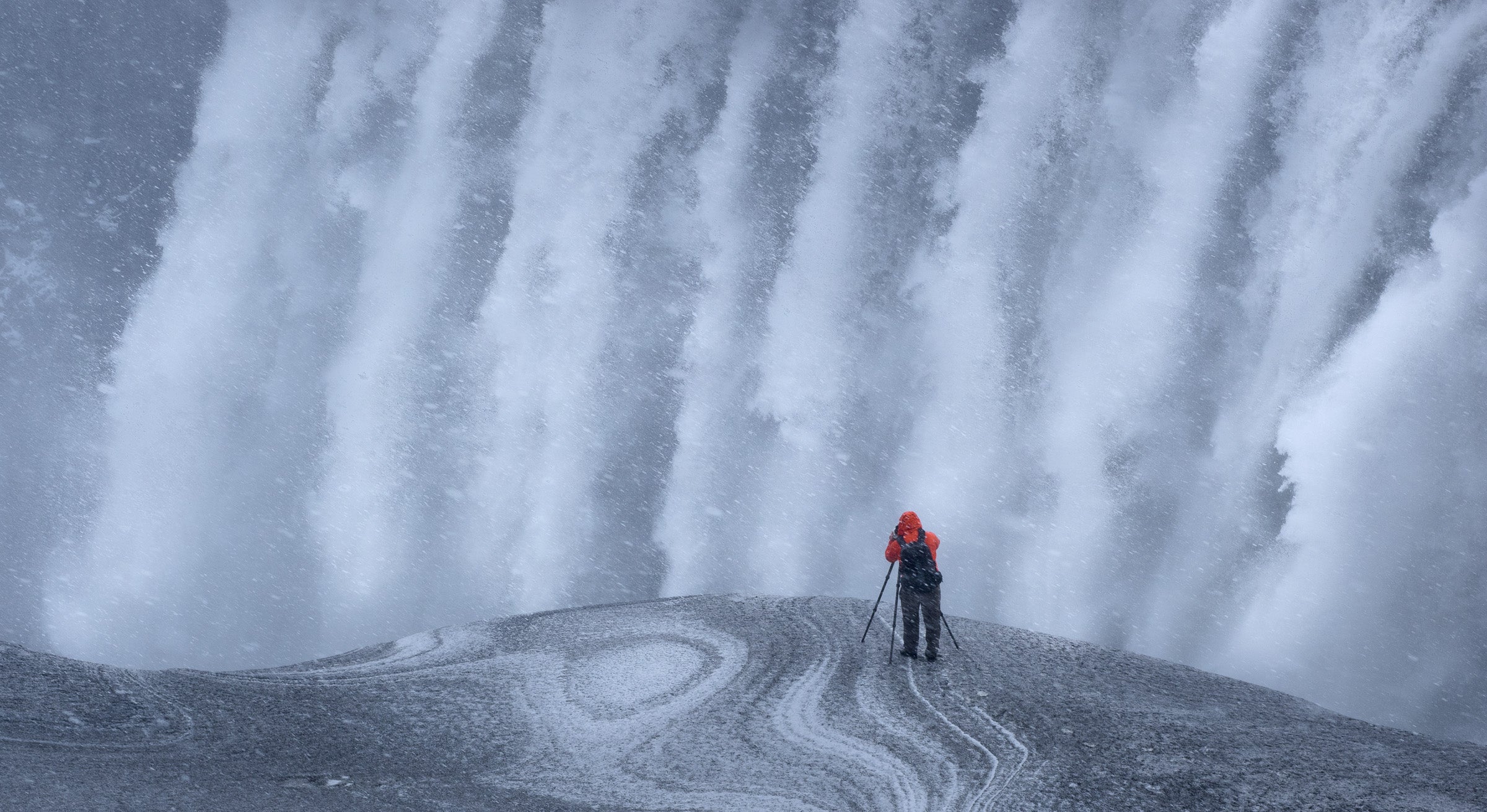 man taking a photo of a waterfall in a snow storm