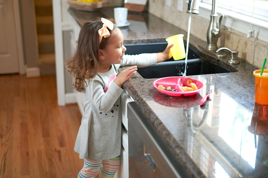 little girl standing at kitchen sink filling water cup