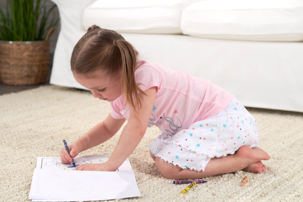 little girl sits on rug with coloring book and blue crayon