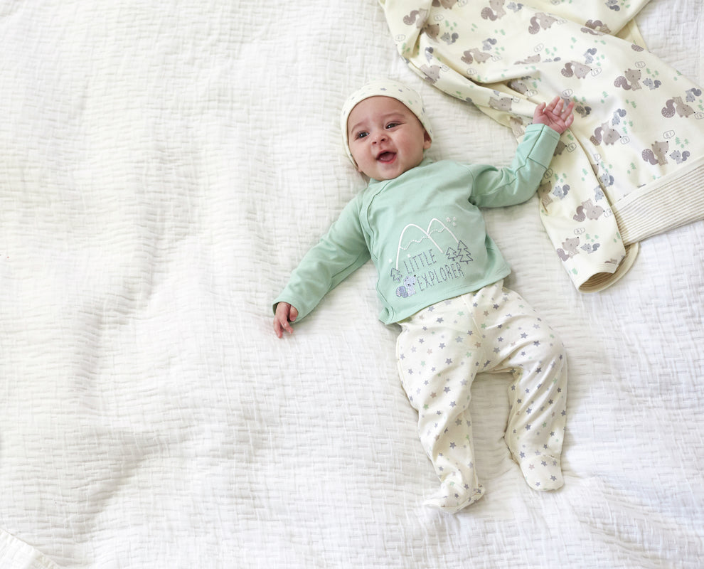 baby laying on white blanket in green outfit, smiling