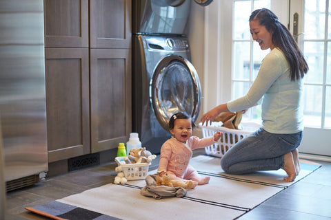 A woman and her adorable baby sitting on the floor, captivated by the washing machine in front of them.