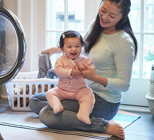 A heartwarming scene of a woman and baby sitting beside a washing machine, creating a bond through everyday chores.