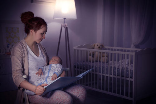 Mom reading to newborn baby in nursery.