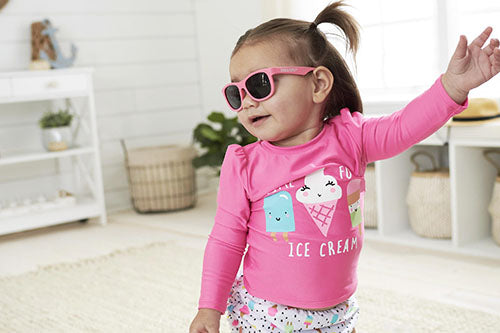 Silly toddler girl in pink top wearing sunglasses.