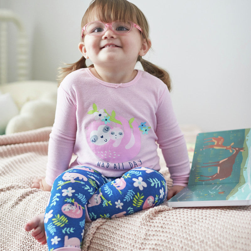 Smiling toddler girl with glasses on bed wearing pink and blue outfit