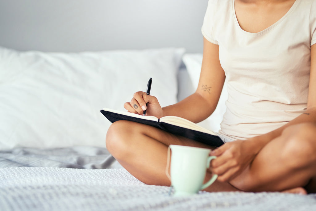 woman writing down positive thoughts before sleep in a journal
