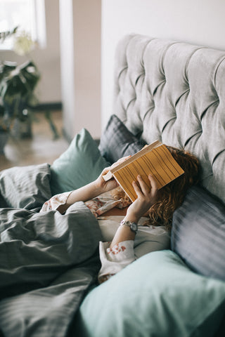 woman covering face with book in bed