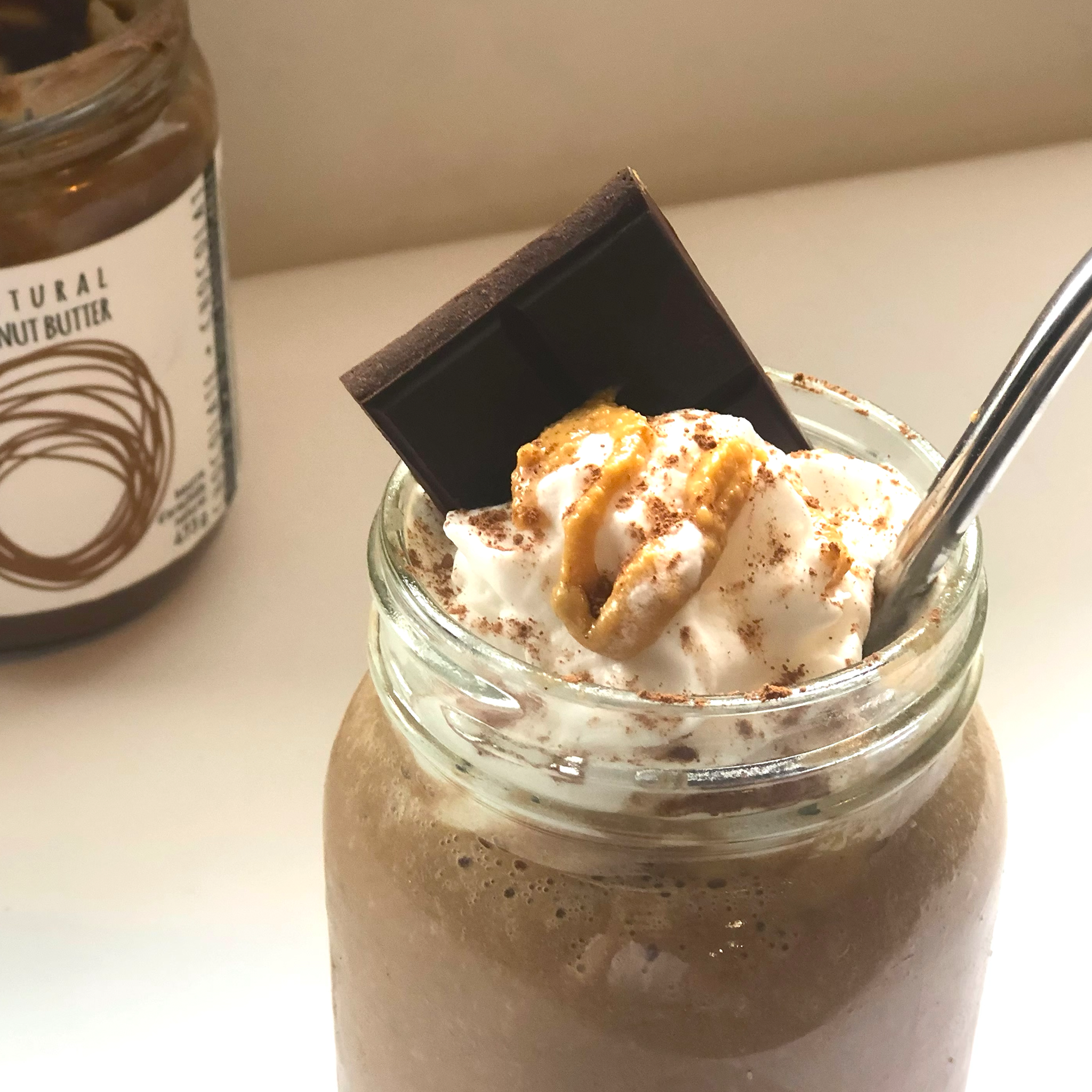 Frozen mocha milkshake with reusable straw, whipped cream and drizzled with natural peanut butter.