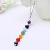 Pendentif collier 7 chakras “équilibre” sur une table blanche avec pot de fleur Kaosix