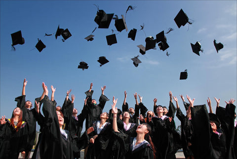 the image shows A collection of students, all dressed in gowns, throwing their graduation hats into the air