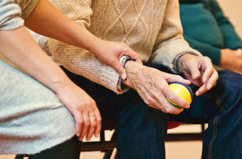 the image shows A close up of people sitting down. A hand gently rests on another person's arm in a caring position