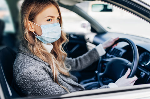 the image shows a woman wearing a facemask driving a car