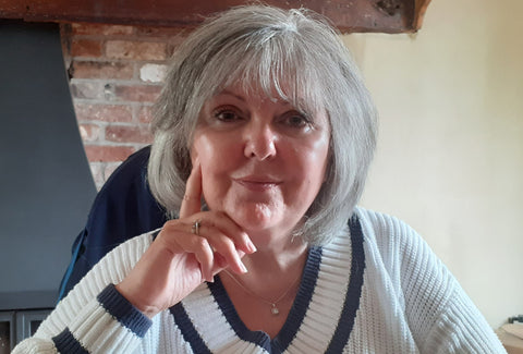 A close-up of Lesley. She sits in front of a brick fireplace and is resting her head on her hands