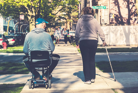 the image shows a man on a walker with a woman using a walking stick