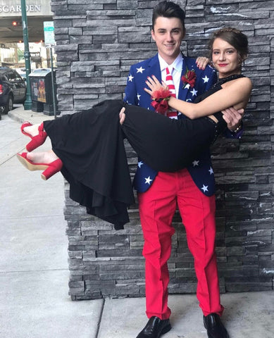 XO Babe, Sav, is being held by her date. She is wearing an all black gown, with bright red heels on. Her date is wearing a tux that has an American Flag print on it.