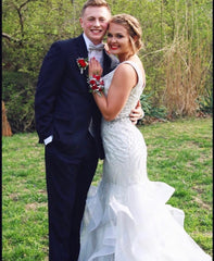 XO Babe, Liv, is posing with her prom date. She is in a silver mermaid gown and he is wearing a black tux. She has on a bright red corsage and he is wearing a red tie.