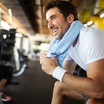 Healthy man in 30s with blue towel around neck sitting at gym