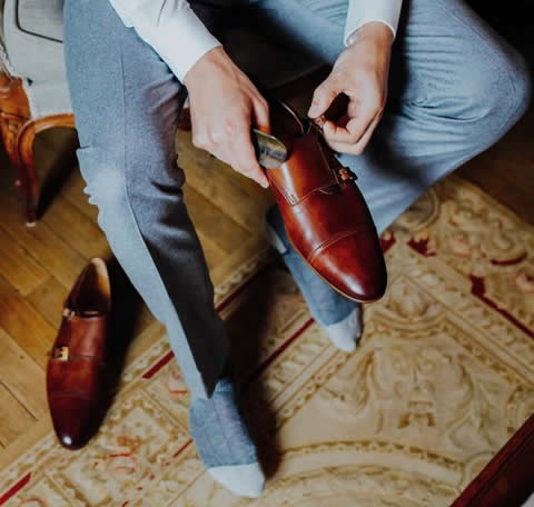 Groom wearing tan monks with light blue/grey suit