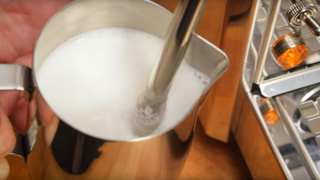 Steam wand frothing milk in a stainless steel frothing pitcher