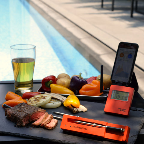 The MeatStick WiFi Bridge Set with assorted Veggies, a Glass of Wine and a Smartphone in Pool Area