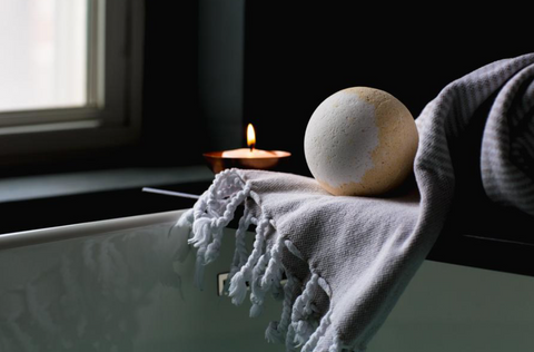 Planet Yum Milk & Honey Bath Bomb hovering over a hot bath with a glowing candle nearby