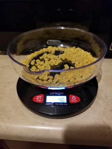 The Truweigh Vortex kitchen scale is turn on and sitting on a counter. It has a serving of dry shell pasta, weighing 40 grams.