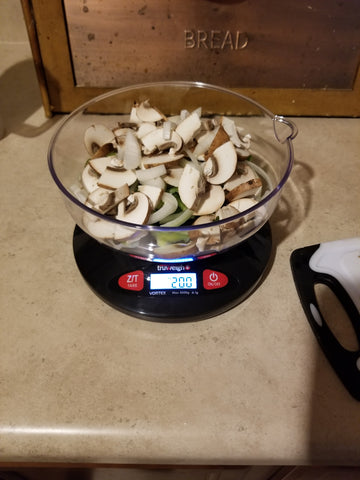 The Truweigh Vortex kitchen scale is turned on and sitting on a counter. It is filled with sliced mushrooms, green peppers and onions, weighing 200 grams.