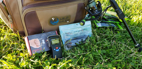 The Truweigh Force Digital Hanging Scale sits among a pile of fishing gear, arranged neatly in front of a large, tan tackle box.