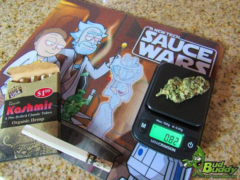 The Truweigh Mini Crimson digital scale is weighing a large cannabis nug that weighs 0.82 grams. The scale is on a Rick and Morty Sauce Wars dab mat, with a box of Kashmir pre-rolled cones laying next to it.