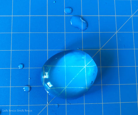 An edible water bubble is sitting on a blue graph background with several water drop surrounding it. Credit to Left Brain Craft Brain