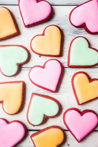 Red Velvet Valentine's Day heart-shaped cookies are arranged in a single layer on a tray. The cookies have pink, yellow, or green frosting. Photo credit to Baking a Moment blog.